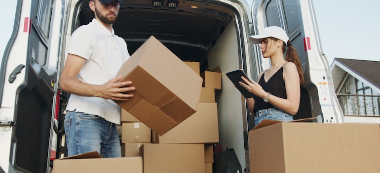 Professional mover loading a van and a woman looking at a notepad