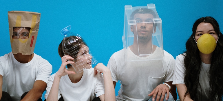 Four people with a paper bag, a plastic bottle, a plastic container, and a plastic face mask on their heads