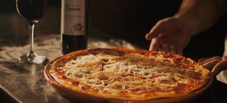 An image of pizza next to a bottle of red wine and a glass