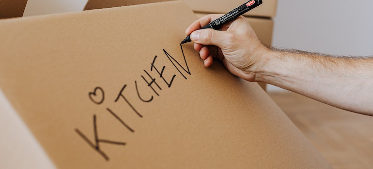 A person writing the word kitchen on a cardboard box