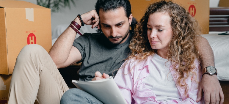 A couple sitting among boxes and looking at the moving checklist