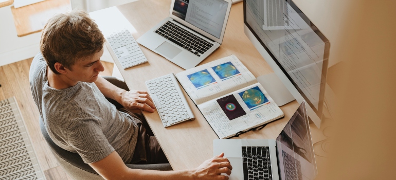 A person with two laptops and a desktop computer in front of him working from home