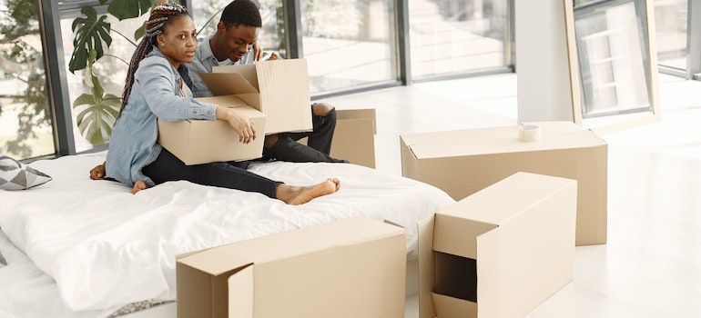 A Young Couple Holding Cardboard Boxes while Sitting on a Bed showing the need to minimize waste when packing for your NYC move.