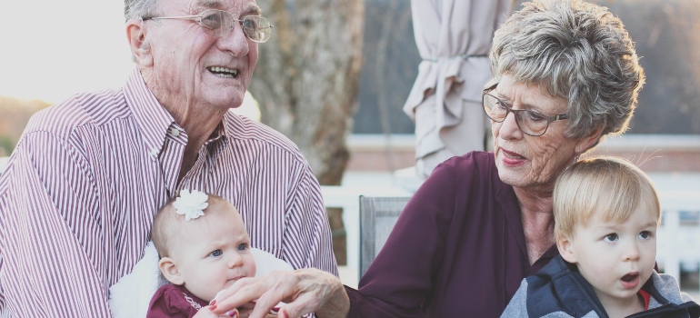 An elderly couple holding their grandkids on their laps representing spending time with family before senior moving