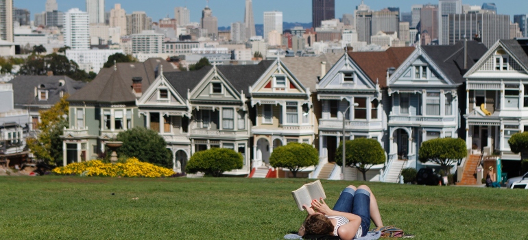 A person lying on the grass reading a book and a view of houses