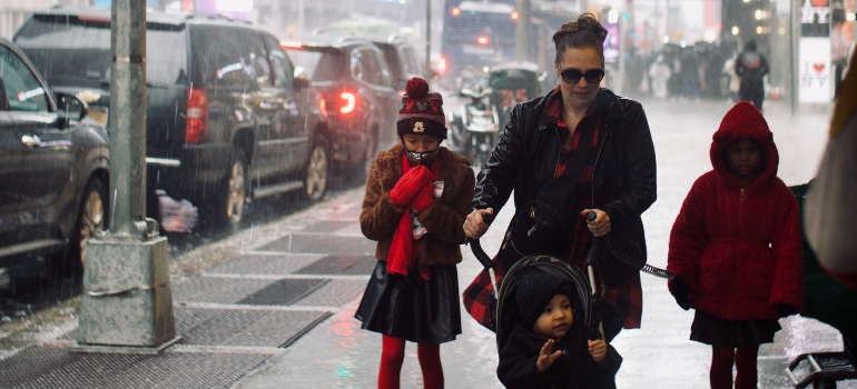 A woman pushing a stroller and two kinds walking beside her