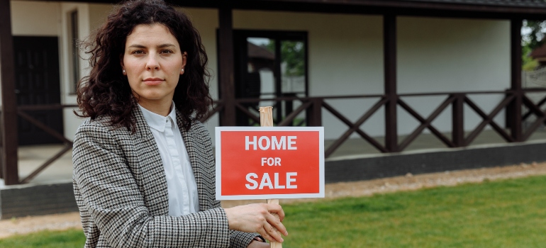 A woman holding a home for sale sign