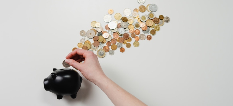 A hand placing a coin in a piggy bank resulting in affordability as one of the  Reasons to move to Sunset Park