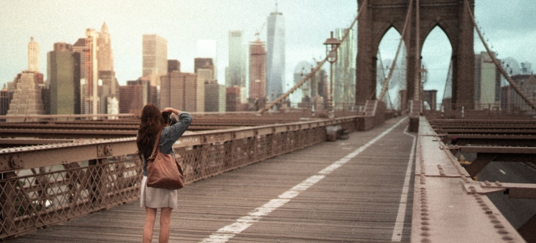 A woman on a Brooklyn Bridge taking a photo of one of the best Brooklyn neighborhoods for young families