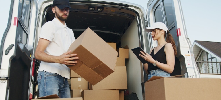 two people surrounded by boxes next to a moving van trying to handle a small move