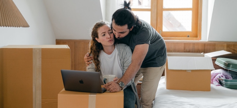 a couple surrounded by boxes looking at a laptop