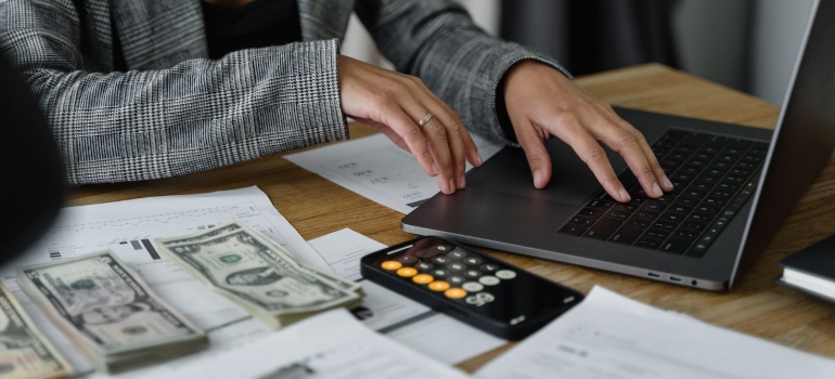 a woman typing on a laptop with money and calculator next to the laptop