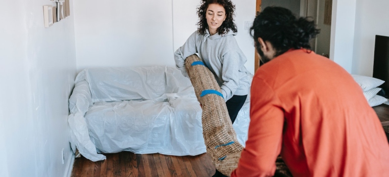 a couple lifting a carpet talking about storing carpets when moving from NY to Florida