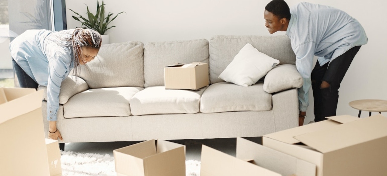 a couple lifting a sofa surrounded by boxes 