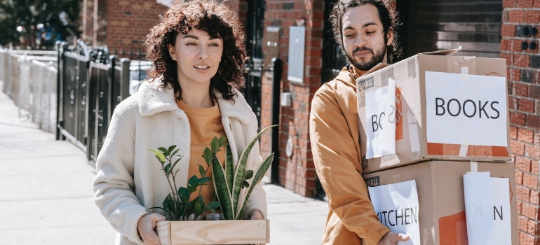 A couple moving , a woman carryring plants and a ,man carrying boxes